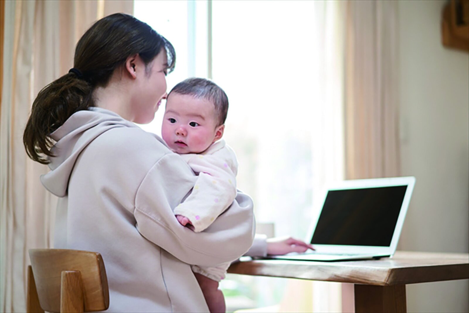 赤ちゃんを抱きながらパソコンで在宅ワークをする様子